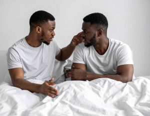 A Black gay couple arguing in bed, unhappy, depicting the impact of top and bottom role dynamics among Black gay men